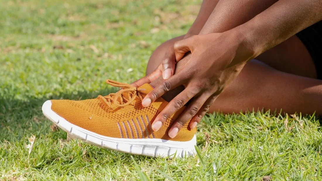 Coureur touchant son tibia douloureux après une course, gros plan sur la jambe et le geste